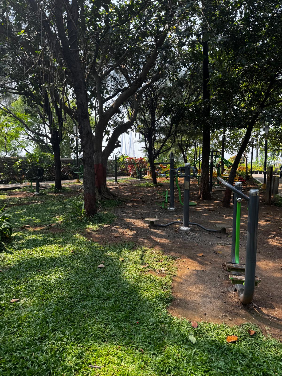 A shaded garden with outdoor exercise equipment near the Bandra waterfront