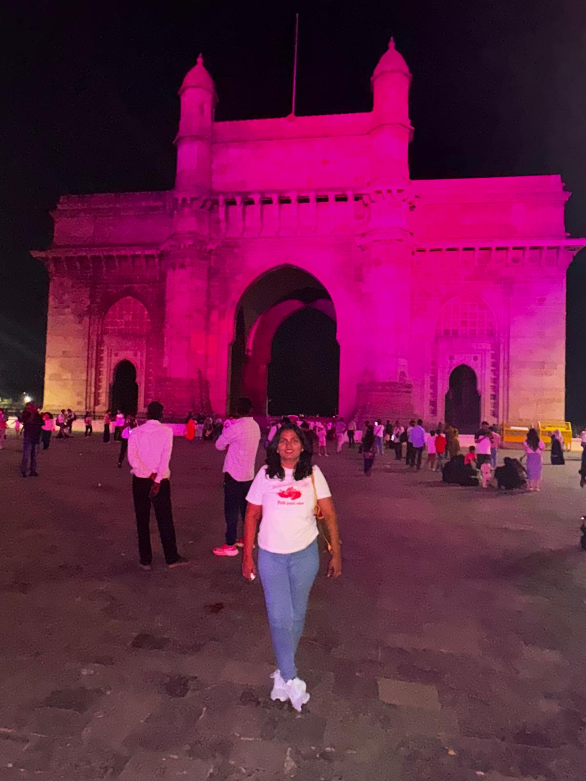 Visitors at the Gateway of India illuminated in pink at night