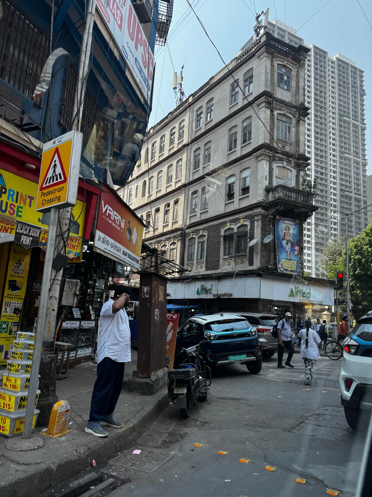 An older Mumbai street-corner building with a newer residential high-rise behind it